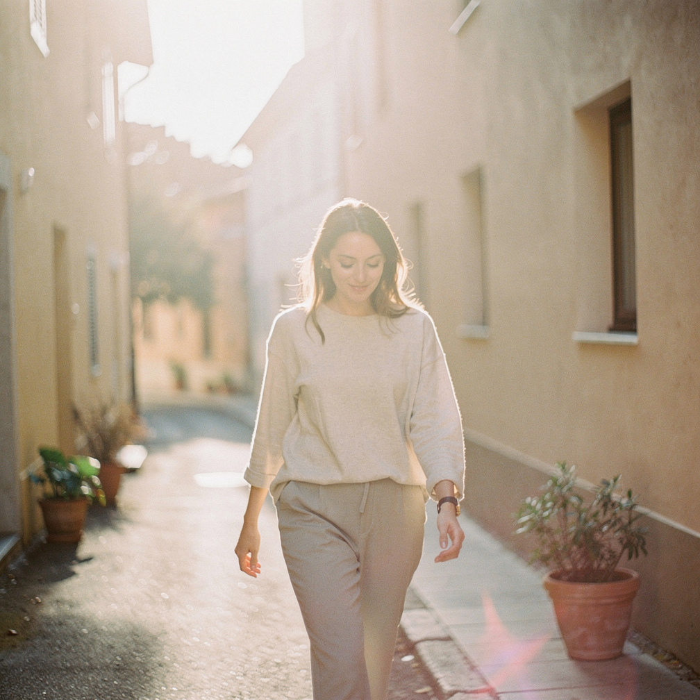Free AI photo: Soft Light European Street Scene. A woman walks alone in a quiet street surrounded by soft natural light.. Categories: Architecture, Fashion, Photography. Colour: Orange.